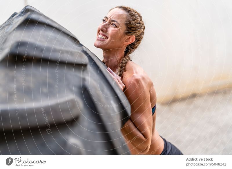 Weibliche Athletin hebt schweren Reifen Sportlerin heben Übung Fitness Training Straße intensiv anstrengen Frau riesig Aktivität stark Wand Kraft physisch