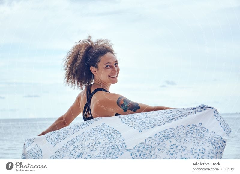 Zufriedene Frau mit wehendem Schal am Meeresufer Glück Wind Freiheit Strand Küstenlinie heiter Sommer positiv Strandbekleidung winken Stoff hispanisch