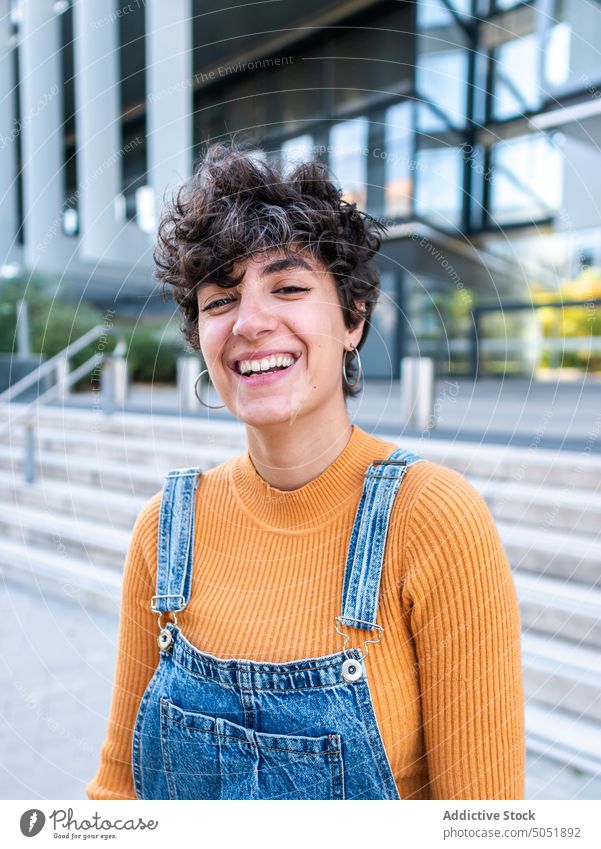 Erfreute Frau steht auf einer Veranda in der Nähe eines modernen Gebäudes Treppenhaus Reling Außenseite Zaun Kälte heiter Straße Sommer urban Stil Großstadt