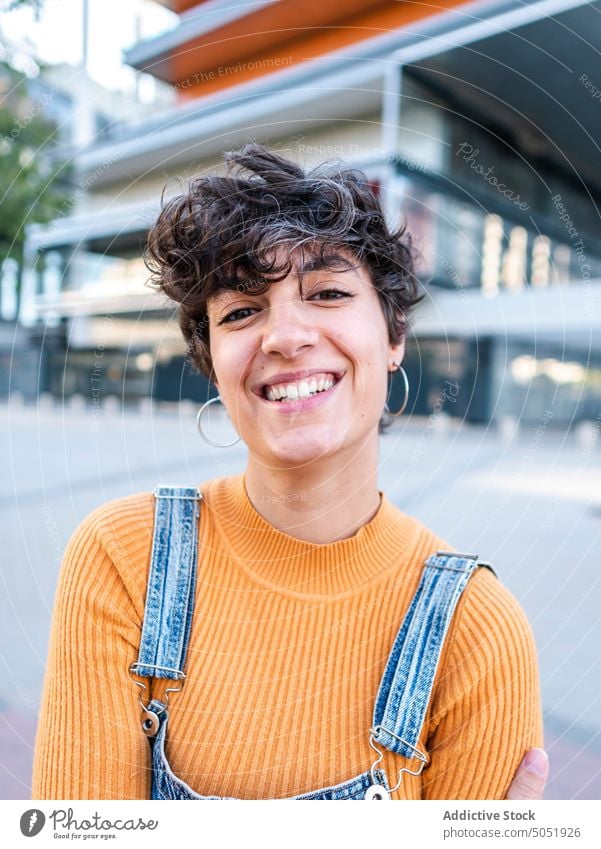 Erfreute Frau steht auf einer Veranda in der Nähe eines modernen Gebäudes Treppenhaus Reling Außenseite Zaun Kälte heiter Straße Sommer urban Stil Großstadt