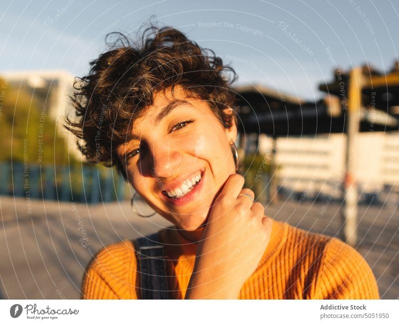 Glückliche Frau auf sonniger Straße stehend Windstille Sonnenlicht lässig Schatten Großstadt urban Lächeln Persönlichkeit allein Kurze Haare Individualität