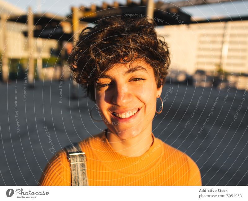 Glückliche Frau auf sonniger Straße stehend Windstille Sonnenlicht lässig Schatten Großstadt urban Lächeln Persönlichkeit allein Kurze Haare Individualität