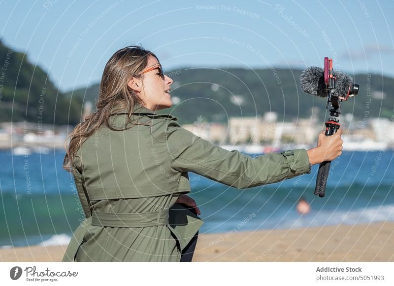 Frau, die am Strand eine Kamera mit Mikrofon aufnimmt Aufzeichnen Video vlog fotografieren Fotokamera Gerät MEER Großstadt Vlogger Selfie Influencer Fotoapparat