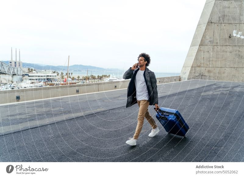 Schwarzer Tourist spricht in der Stadt mit Smartphone Mann Koffer reden Spaziergang Urlaub Großstadt Ausflug benutzend Telefonanruf Reisender sprechen männlich