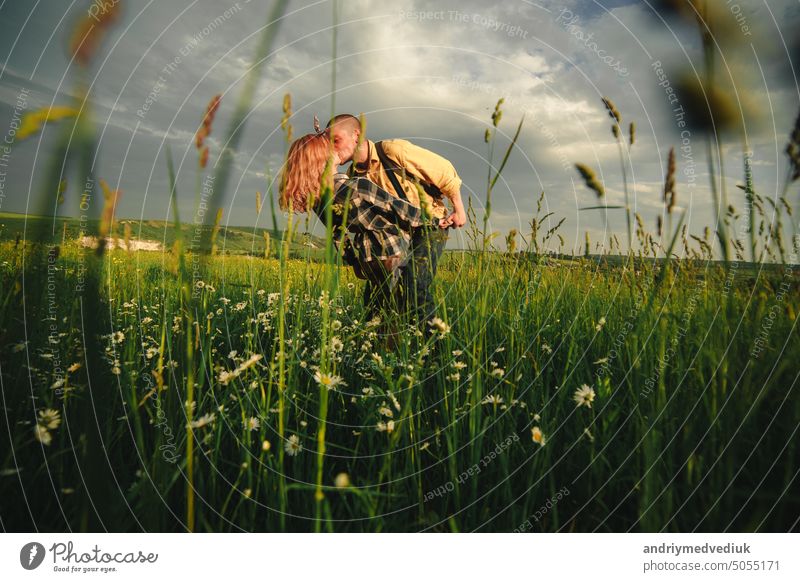 Verliebtes Hipster-Paar, das im Feld spazieren geht, sich küsst und die Hände hält, sich umarmt, im Sommer bei Sonnenuntergang im Gras liegt. valentines day