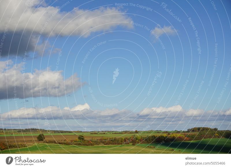 Vorgebirgslage mit herbstlichen Feldern und Bäumen, blauem Himmel mit Schönwetterwolken und einem Windpark am Horizont Vorgebirge Windräder Herbst Fernsicht