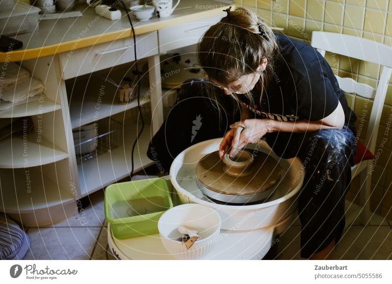 Töpfern, Frau in ihrer Töpferwerkstatt formt konzentriert ein Gefäß aus Ton auf der Töpferscheibe Wände hochziehen pulling walls Hände Handwerk Hobby Kunst