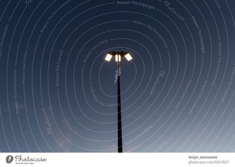 Ein angeschalteter Flutlichtmast auf einer Sportstätte aus der Entfernung. Dunkelheit, ein paar Wolken sind am Himmel zu erkennen Lampe Licht Beleuchtung