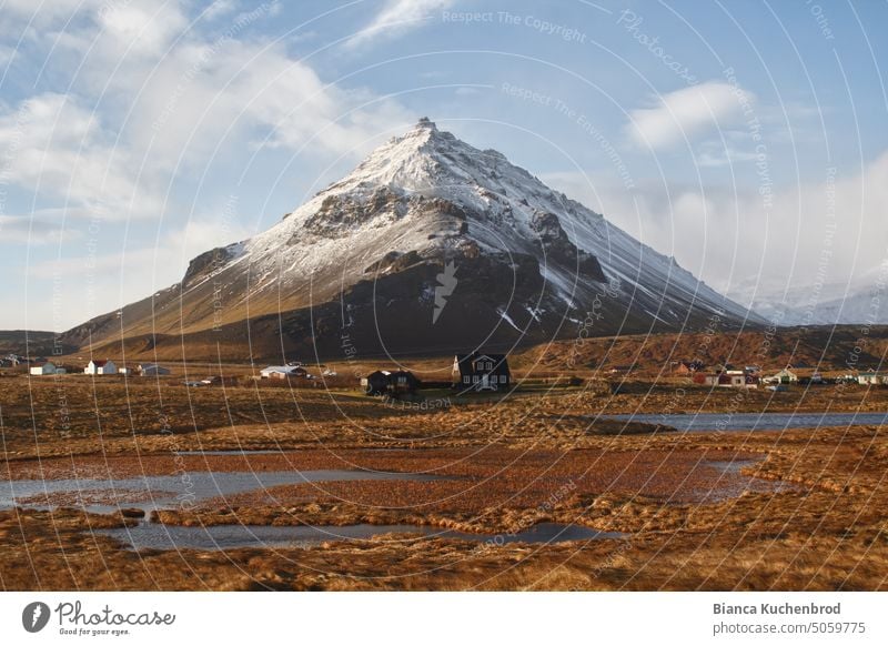 Ein schneebedeckter Berg in Island mit einigen kleinen Häusern am Fuße in Snaefellsnes. Berge u. Gebirge Isländischer Berg Landschaft Snæfellsnes Himmel Wolken