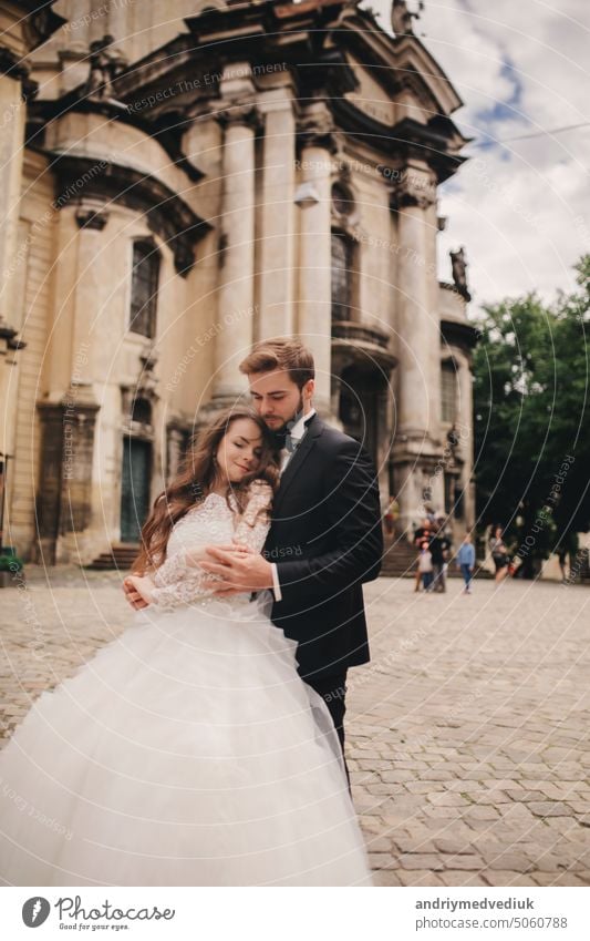 Stilvolle Braut und Bräutigam sanft umarmt auf europäischen Stadtstraße. Gorgeous Hochzeit Paar von Jungvermählten umarmt in der Nähe von alten Gebäude. romantisch sinnlichen Moment der Jungvermählten