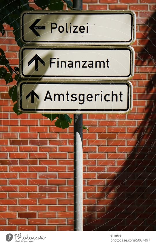 Behördenwegweiser / Schilderbaum mit Hinweisschildern  Polizei  /  Finanzamt  /  Amtsgericht - vor einer roten Ziegelwand / Navigation Orientierung Wegweiser