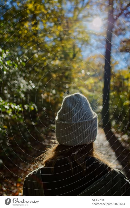 Eine junge Frau mit einer hellen Stickmütze geht einen Waldpfad entlang der hell leuchtenden Sonne entgegen weiblich gehen Waldweg der Sonne entgegen Zukunft