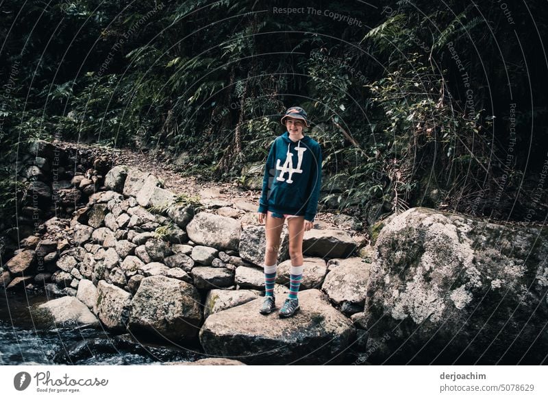 Ein Girl steht an einem Fluss im Urwald. Sie überlegt wie sie trockenden Fußes auf die andere Seite kommt. Flussufer Farbfoto Außenaufnahme Wasser Sommer Natur