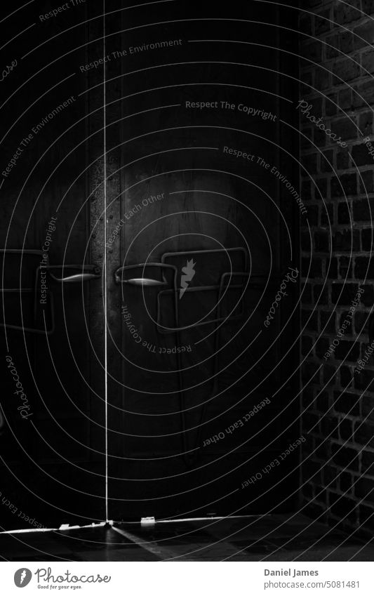 Schwere Metalltüren mit verschlungenen Türgriffen, schummrige Beleuchtung. dunkel Raum Struktur Gebäude düstere Atmosphäre düsterer Schrecken gefangen