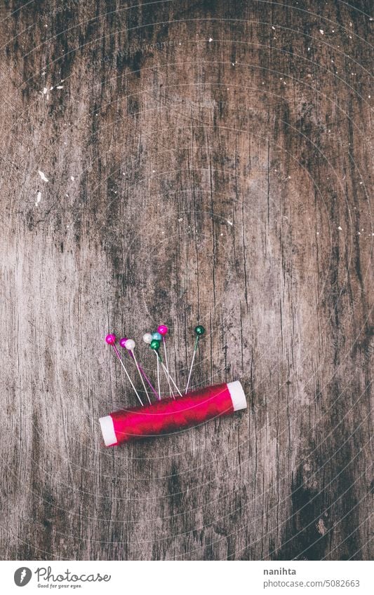 Roter Faden und bunte Nadeln vor einem alten Holzhintergrund rustikal Hintergrund Textur vertikal Stecknadel Faser Farbe farbenfroh mehrfarbig gealtert