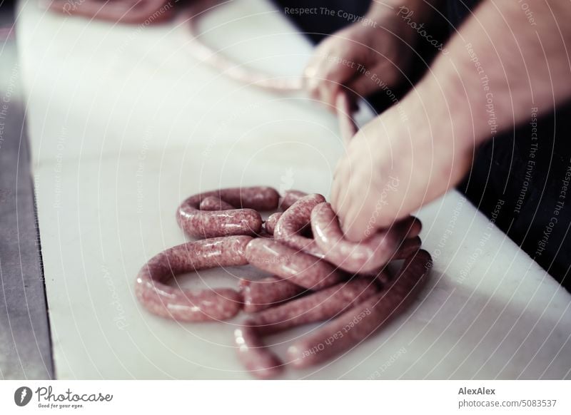 zwei Hände die Wurst herstellen, die gerade aus einer Wurstfüllmaschine kommt. Maschine Handwerk Fleischer Fleischerei Herstellung Produktion