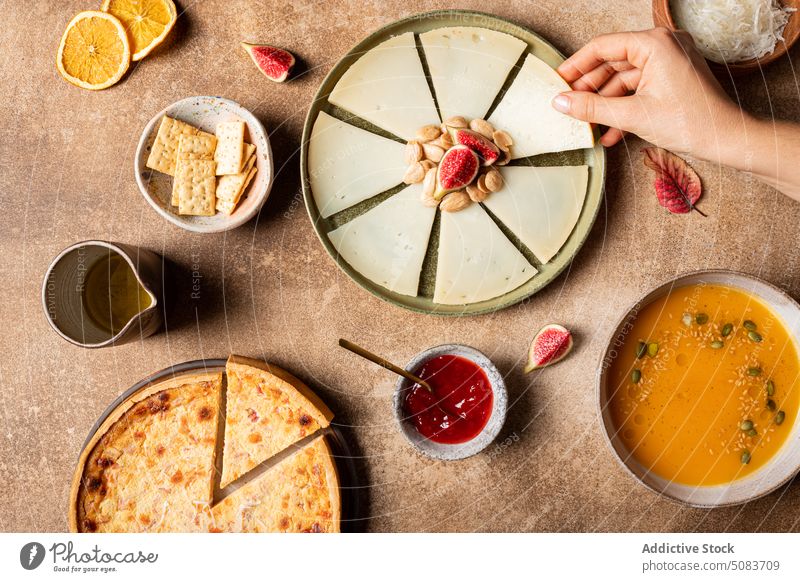 Crop-Frau nimmt ein Stück Käse vom Teller Spielfigur Tisch Nut Feige Pasteten Saucen Cracker Suppe Kürbis Samen Zitrusfrüchte orange dienen Blatt Frucht Speise