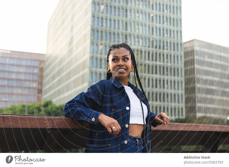 Fröhliche schwarze Frau steht auf einer Brücke gegen den Stadtverkehr Reling Stadtbild Verkehr Gebäude urban Kälte Straße Lächeln positiv Glück Afroamerikaner