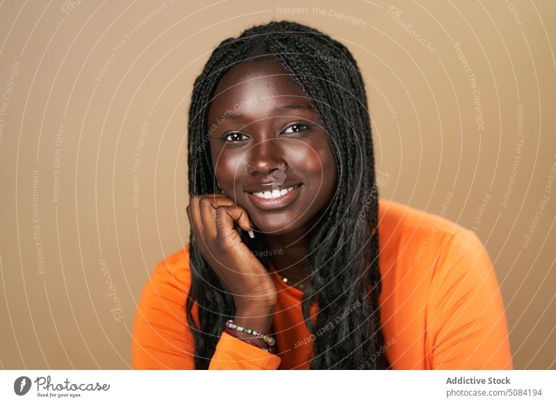 Ruhige glückliche schwarze Frau schaut in die Kamera Model Porträt Lächeln Afro-Zöpfe Vorschein Persönlichkeit Atelier brauner Hintergrund Menschliches Gesicht