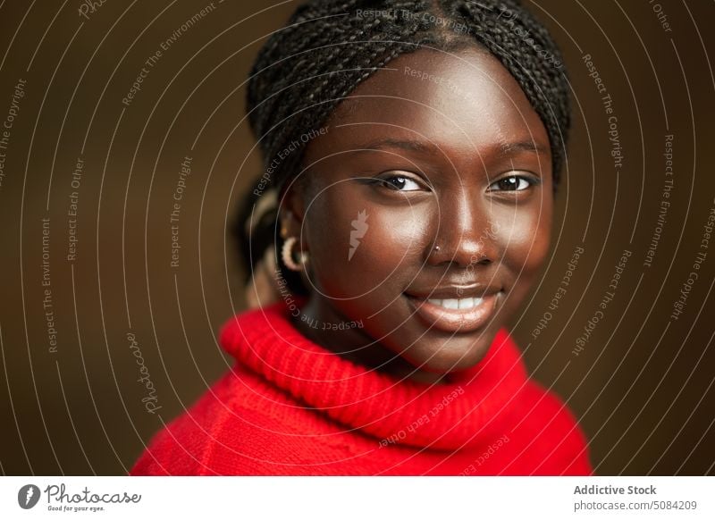 Ruhige glückliche schwarze Frau schaut in die Kamera Model Porträt Lächeln Afro-Zöpfe Vorschein Persönlichkeit Atelier brauner Hintergrund Menschliches Gesicht