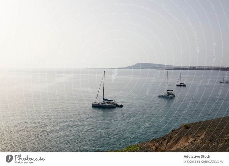 Boote segeln im Meer in der Nähe von felsigen Klippen im Sonnenlicht MEER vulkanisch Segelboot Natur Meereslandschaft Insel malerisch atemberaubend Ufer Küste