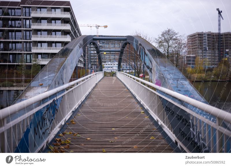 Brücke mit seitlichem Geländer, Bogen, Holzbohlen und Wohnhäusern in städtischer Umgebung Bohlen Flucht Perspektive Blick Dynamik dynamisch modern Architektur