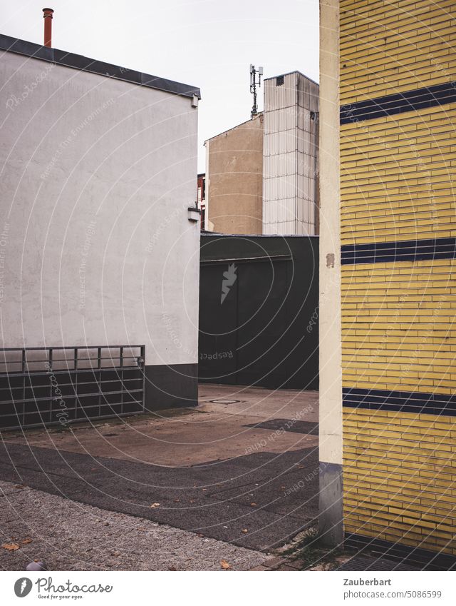 Einfahrt in einen älteren Gewerbehof, Asphalt, Fassaden, Klinker Hinterhof Areal Hof Arbeit Gebäude Wand Bauwerk streng trist geordnet ordentlich Fläche