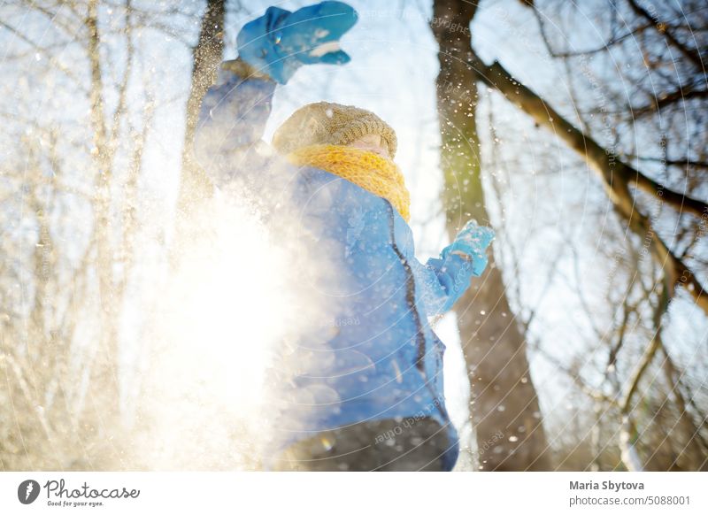 Kleiner Junge wirft frischen Schnee aus seinen Händen. Kind genießen Spaziergang im Park auf verschneiten Tag. Baby mit Spaß während Schneefall. Outdoor-Winter-Aktivitäten für Kinder.