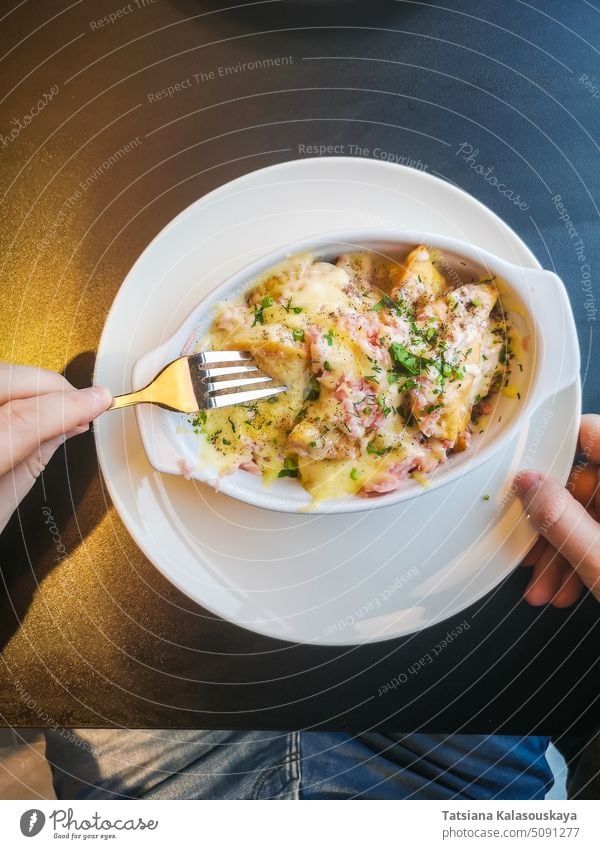 Ein Mann isst gebackene Knödel mit einer Soße aus Speck, Schinken, Kräutern und Käse. essen Saucen Küchenkräuter Hände litauisch national Speise weiß Teller