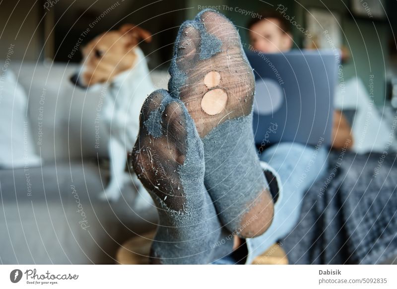 Mann mit undichten Socken, der sich auf dem Sofa neben einem Hund ausruht und einen Laptop benutzt Bein Golfloch Arbeit Krise Menschen Freiberufler schlecht