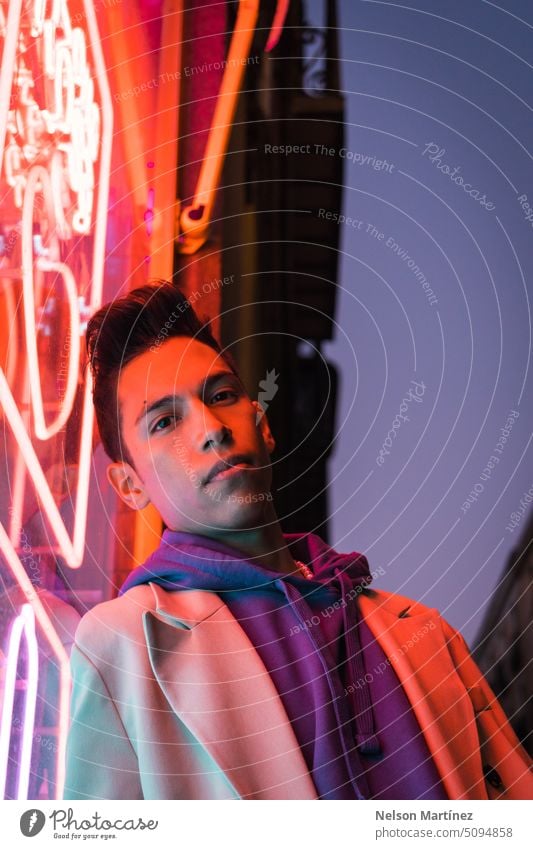 Porträt eines jungen hispanischen Mannes mit rotem Neonlicht im Gesicht, der einen beigen Blazer trägt Straße hell Mode Anzug Party Aussehen Leder Licht Nacht