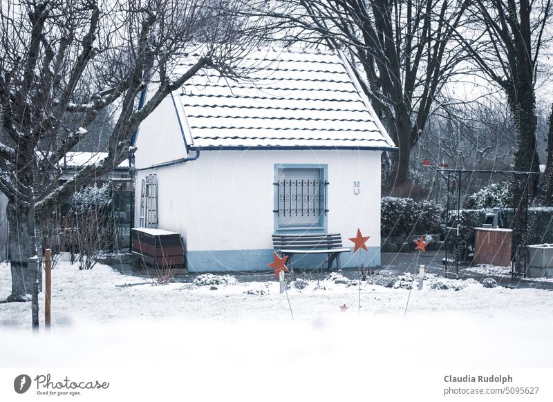 Kleines Gartenhaus an einem verschneiten Wintertag mit roter Sternendekoration im Beet Schrebergarten Schnee schneebedeckt Winterstimmung Garten im Winter