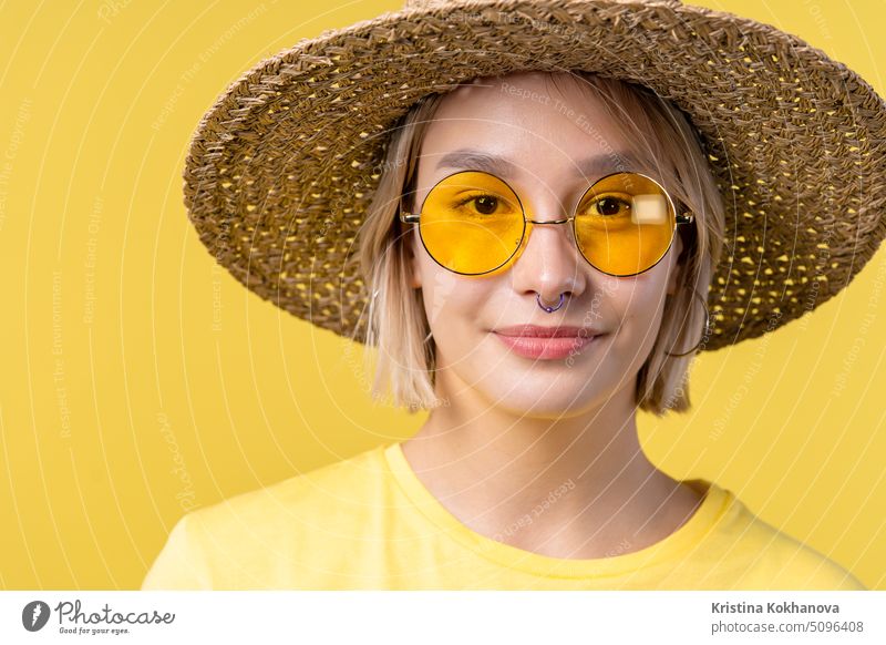 Porträt einer jungen hübschen blonden Frau auf sommerlichem gelben Studiohintergrund. Selbstbewusstes sonniges Outfit mit Sonnenbrille und Strohhut. Erwachsener