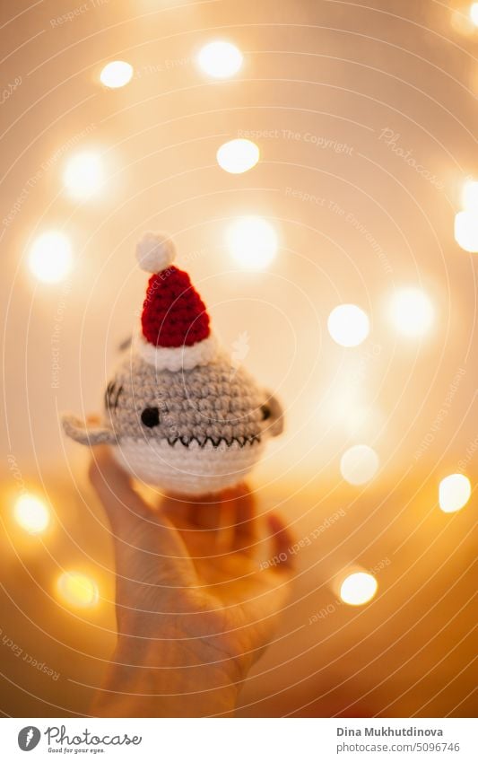 Gehäkelte Plüschhaie mit Weihnachtsmannmützen als Weihnachtsgeschenke. Amigurumi Spielzeug handgefertigt. Häkel-Hobby. Making DIY Geschenke für Familie und Freunde und Kinder. Bokeh Lichter Hintergrund. Handgemachtes Hobby.