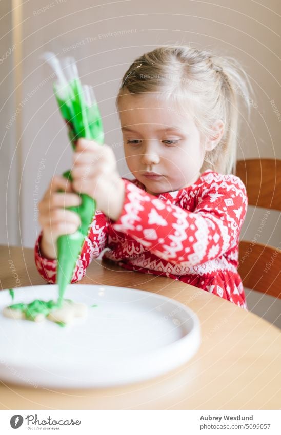 Kleines Mädchen im roten Weihnachtspulli beim Verzieren von Weihnachtsplätzchen Zuckerguß Lebensmittel Lebkuchen selbstgemacht Gebäck Keks süß Feier festlich