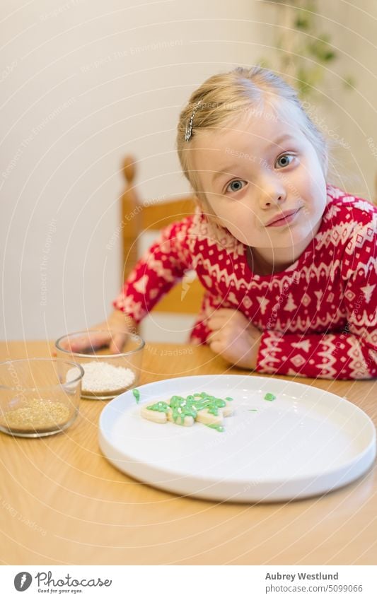 Kleines Mädchen schaut in die Kamera, nachdem sie ihr Weihnachtsplätzchen verziert hat backen Schönheit Feier Kind Kindheit Kinder Weihnachten Weihnachtsbaum