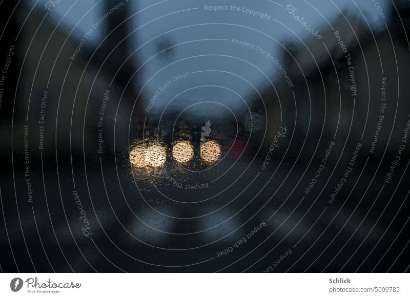 In der Dämmerung im Auto vor einem Fußgängerüberweg bei Regenwetter Windschutzscheibe nass selektiver fokus dunkel Autoscheinwerfer Bokeh Häuser Himmel