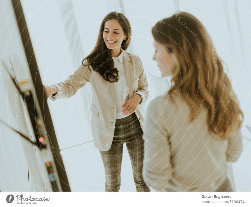 Zwei junge Frauen besprechen die Finanzergebnisse auf dem großen Wandbildschirm im Büro zwei Bildschirm Besprechung Investition Gewinn digital