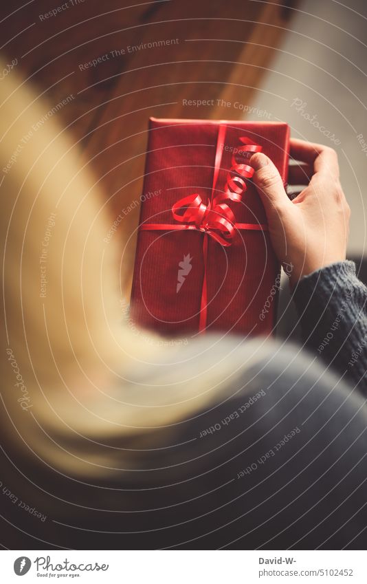 Frau mit einem Geschenk in den Händen Weihnachten Überraschung Geburtstag Herzlichen Glückwunsch Weihnachtsgeschenk Vorfreude Heiligabend Freude rot öffnen