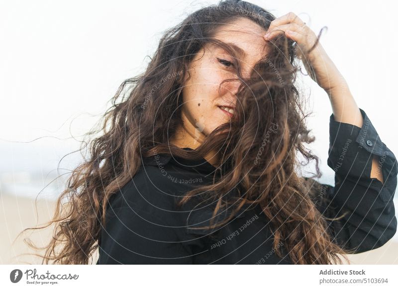 Junge Frau bei windigem Wetter Kokette Persönlichkeit positiv Haare berühren Individualität Vorschein schick Wind Porträt Lächeln heiter brünett Stil idyllisch