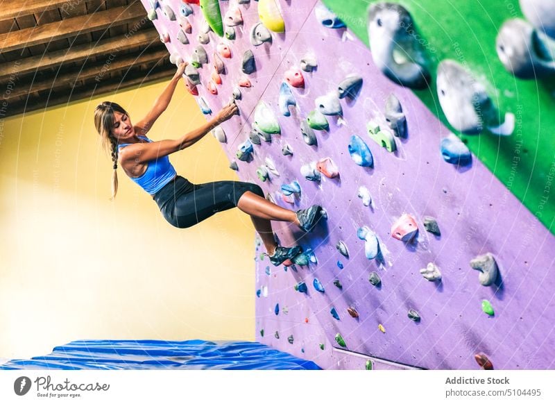 Weibliche Kletterin hängt an schräger Wand Sportlerin hängen Training Aufstieg Neigung Fitnessstudio Griff üben Frau Unterlage Kraft Bouldern extrem Aktivität