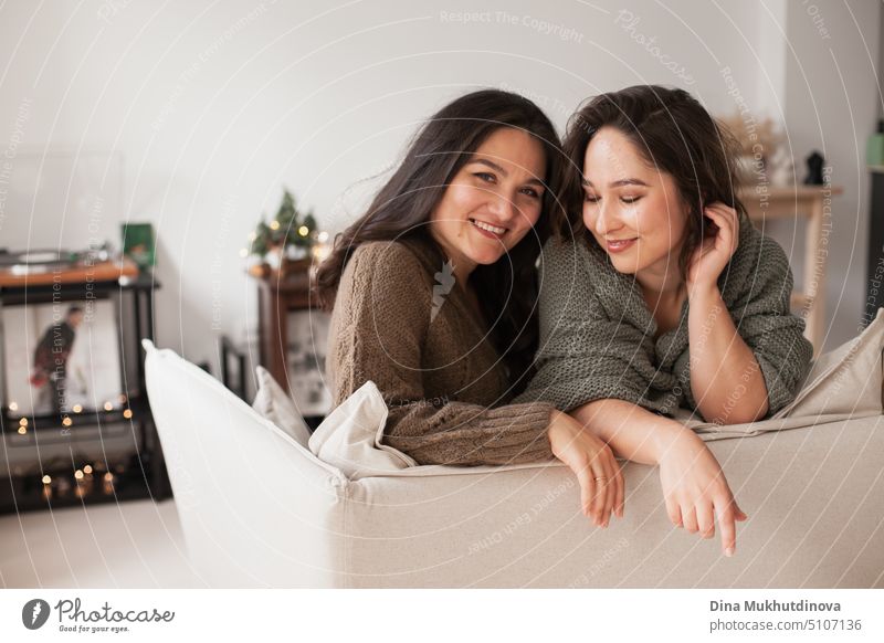 Zwei Frauen sitzen auf einer Couch in einer gemütlichen Wohnung. Familie verbringt Zeit zu Hause. Porträt von Schwestern lächelnd in modernen minimalen Interieur.