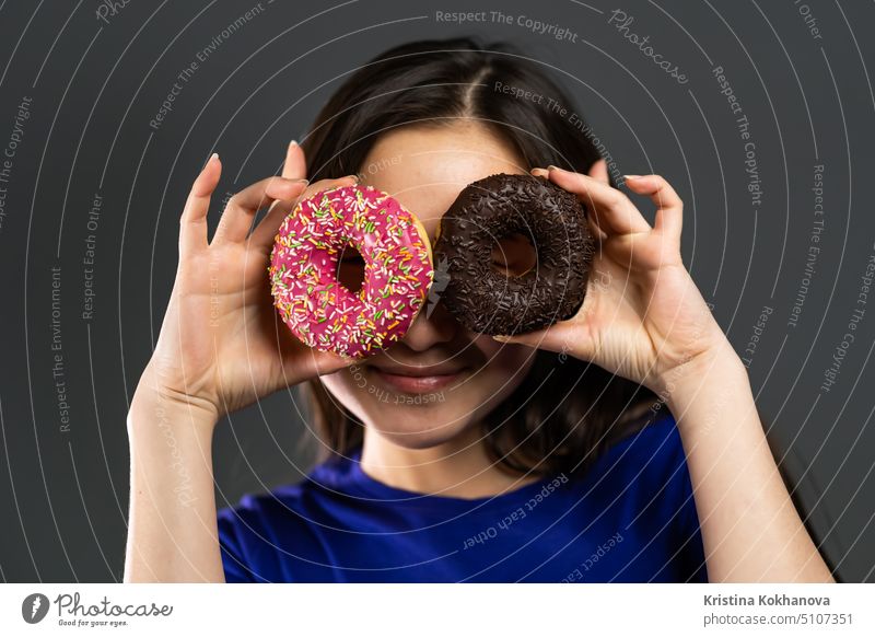 Porträt der fröhlichen schönen asiatischen Frau tanzen mit Süßigkeiten bunte Donuts isoliert auf grauem Hintergrund Studio. Konzept der Freude, Essen, Lebensstil.