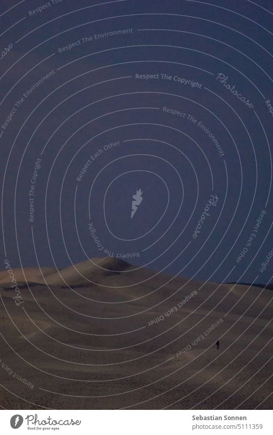 Einsame Silhouette eines Mannes, der auf der riesigen Sandformation Dune du Pilat spazieren geht, beleuchtet durch das Mondlicht in der Nacht, Arcachon, Nouvelle-Aquitaine, Frankreich