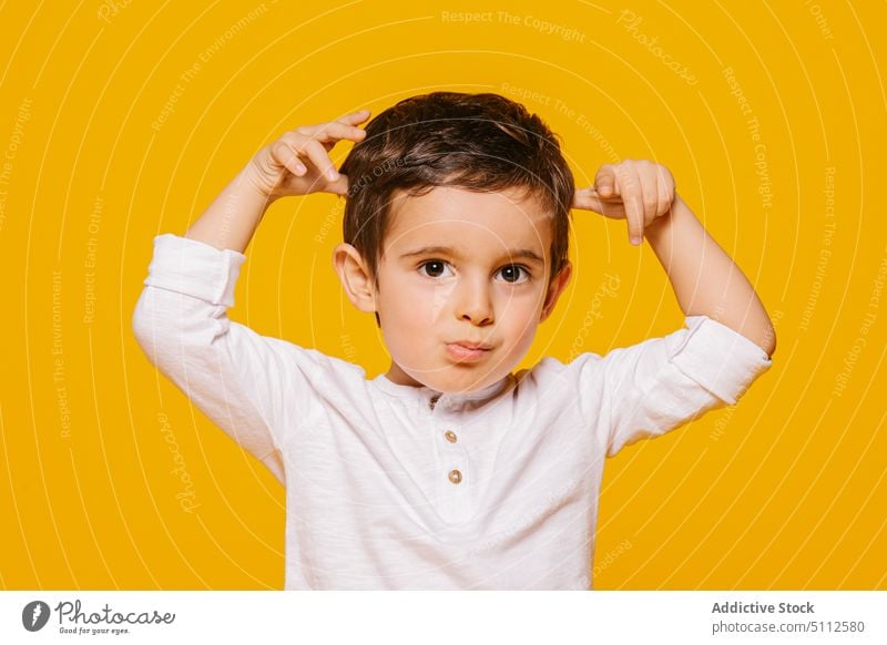 Süßer Junge berührt Haare und schaut in die Kamera und schaut in die Kamera Kind Mädchen niedlich gestikulieren lässig wenig erstaunt bezaubernd Kindheit Glück