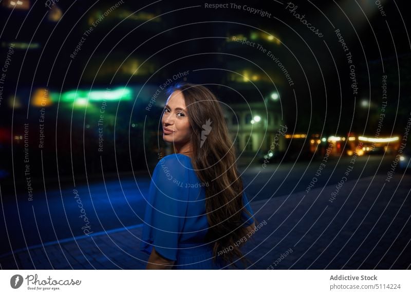 Junge Frau schaut über die Schulter in die Kamera Straße dunkel Nacht Stil Nachtleben brünett urban Vorschein Porträt jung trendy feminin lange Haare Kleid