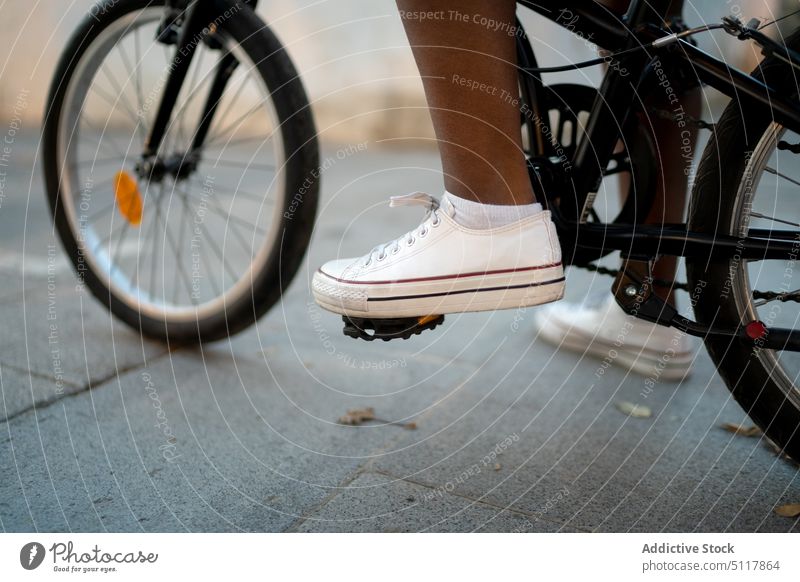 Crop schwarze Frau auf Fahrrad Schritt Pedal Straßenbelag Arbeitsweg Mitfahrgelegenheit urban Turnschuh Afroamerikaner Stil Bürgersteig umweltfreundlich