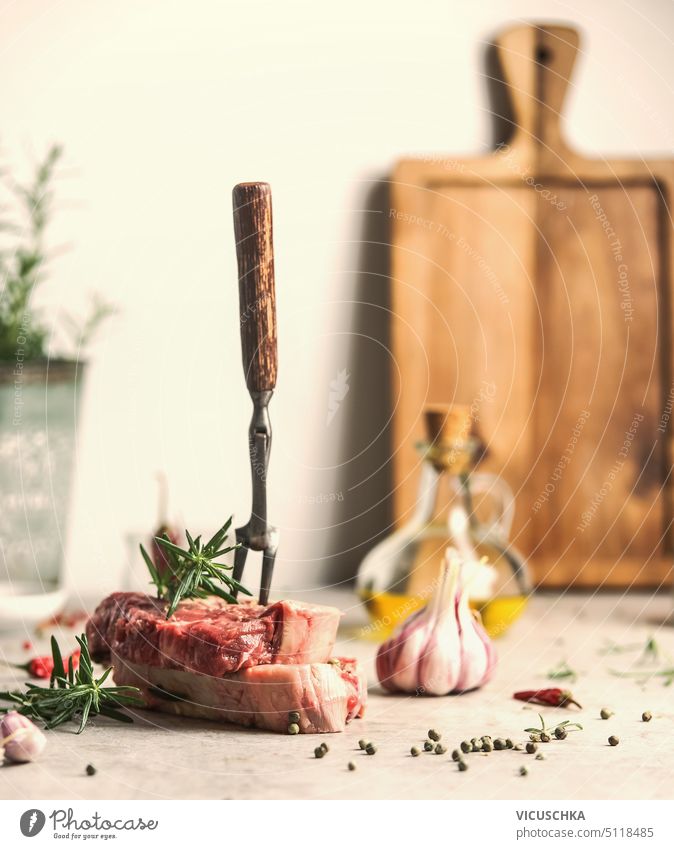 Rohe Rindersteaks mit Fleischgabel, Kräutern und Gewürzen auf dem Küchentisch, Vorderansicht roh Rindfleisch Steaks Küchenkräuter Tisch Knoblauch angus Filet