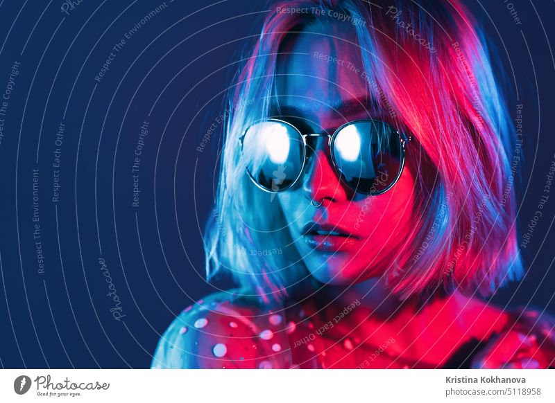 Close up Porträt der Millennial hübsches Mädchen mit kurzer Frisur mit Neonlicht. Gefärbte blaue und rosa Haare. Mysteriöser Hipster-Teenager mit Brille. Licht