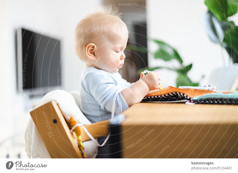 Glückliches Kleinkind sitzt am Esstisch und spielt mit seinem Spielzeug in traditionellen skandinavischen Designer-Holzstuhl in modernen hellen atic Hause. Niedliches Baby spielt mit Spielzeug